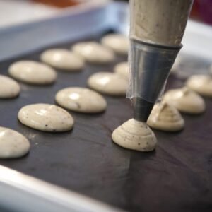 Piping bag piping macaron batter onto a baking tray
