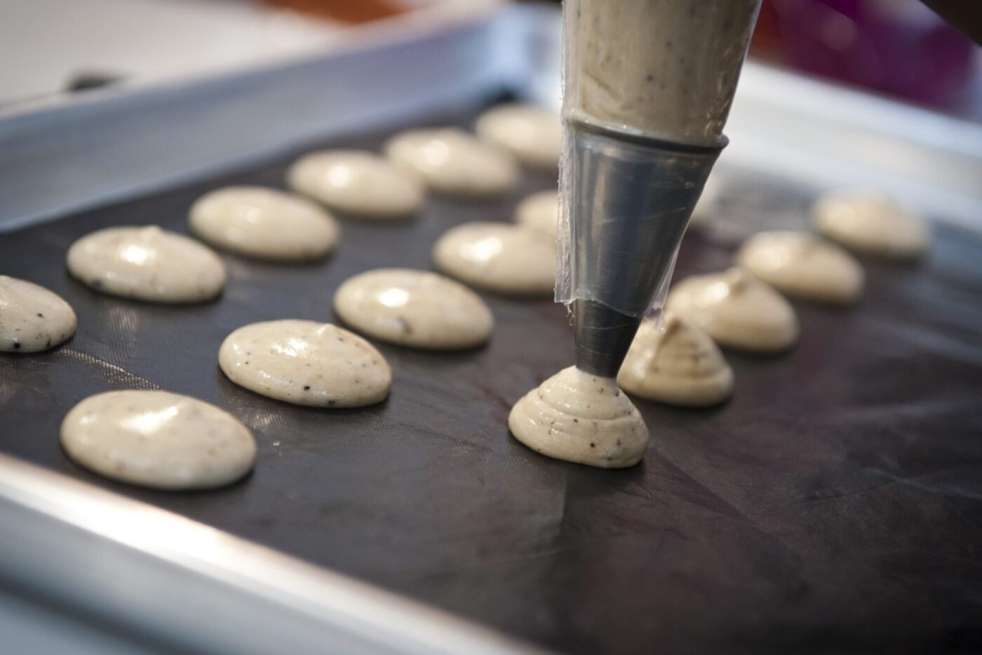 Piping bag piping macaron batter onto a baking tray